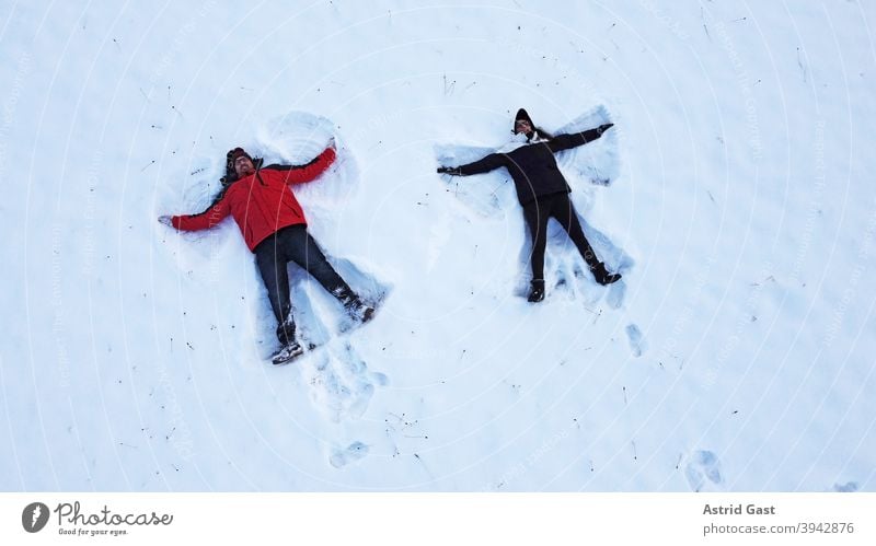 Drohnenaufnahme von einer Frau und einem Mann, die im Winter auf dem Boden liegend einen Schnee-Engel machen luftaufnahme drohnenfoto frau mann winter schnee