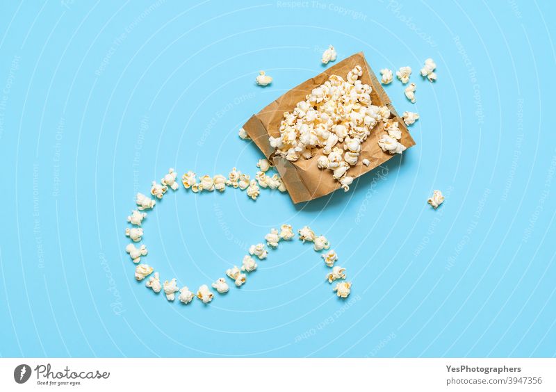 Popcorn in einer Papiertüte isoliert auf blauem Hintergrund. Popcorn-Tüte explodiert, Ansicht von oben Überfluss Amuse-Gueule Blauer Hintergrund butterartig