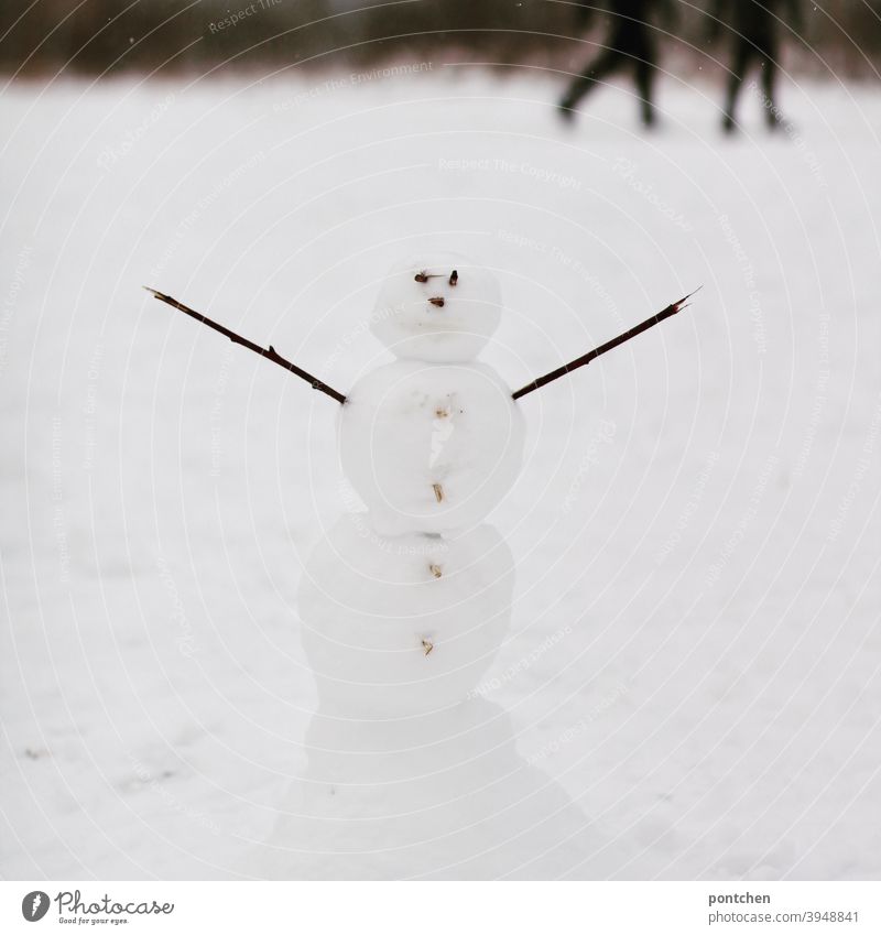 Ein Schneemann mit ausgestreckten Armen steht im Schnee. Verschwommene Spaziergänger im Hintergrund. Winter schnee winter kinderspiel freude spaß vergnügen kalt