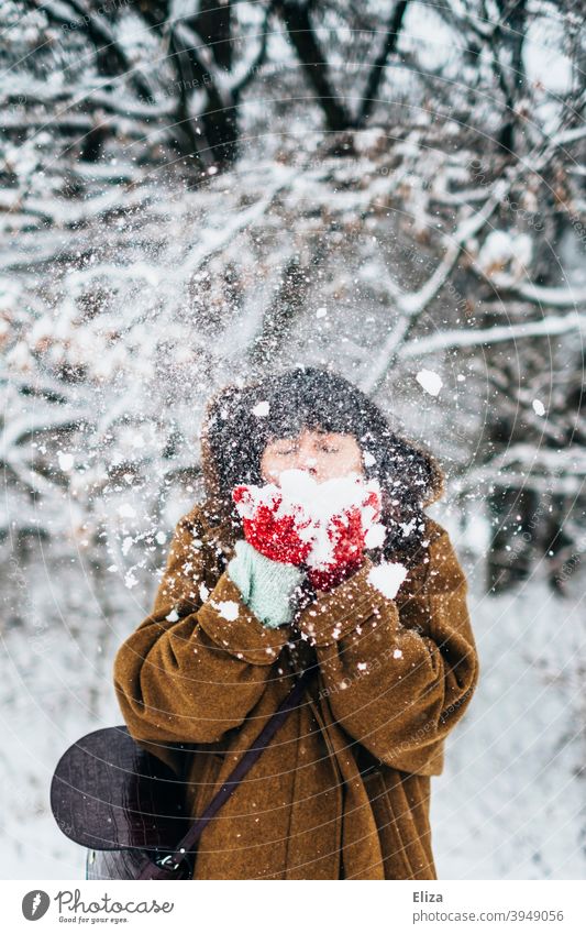 Frau pustet Schnee im Winter Freude Schneelandschaft verschneit Natur draußen kalt weiß Winterstimmung Winterwald Wintertag Handschuhe Mantel jung winterlich