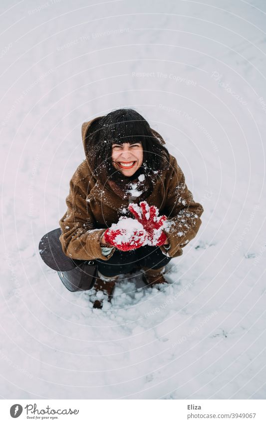 Eine Frau sitzt im Schnee, formt einen Schneeball und grinst frech verschmitzt schelmisch lachen grinsen Spaß Winter Schneeballschlacht lustig Freude neckisch