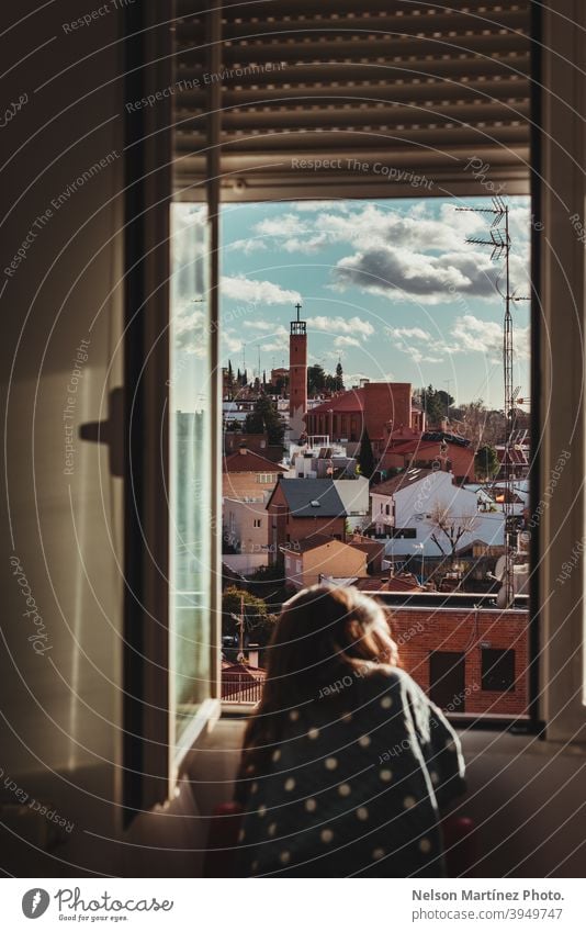 Schöne Aufnahme eines kleinen Mädchens mit dunklen Haaren, das an einem sonnigen Tag aus dem Fenster schaut. Porträt Kind Childhod heimwärts Viertel