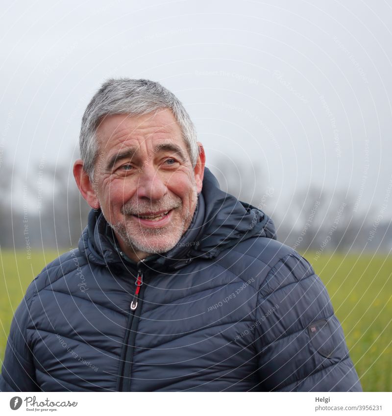 Porträt eines männlichen Seniors in blauer Steppjacke, der lächelnd zur Seite schaut Mensch Mann 60+ draußen Winter Jacke grauhaarig kurzhaarig Bart