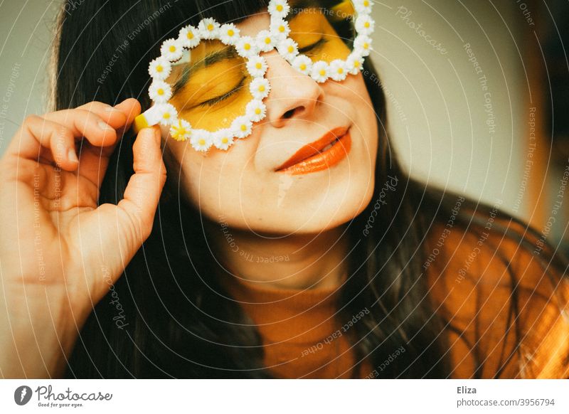 Frau mit Blümchen-Sonnenbrille im Sonnenlicht. Retrostimmung, Optimismus gute Laune und Sommer. Sommerstimmung Frühling Sonnenschein farbenfroh gelb orange