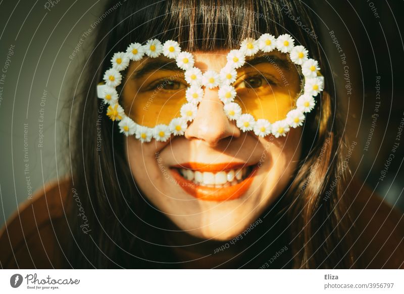 Lachende Frau mit Blümchen-Sonnenbrille im Sonnenlicht. Retrostimmung, gute Laune, Optimismus und Sommer. Sommerstimmung Frühling Sonnenschein farbenfroh gelb