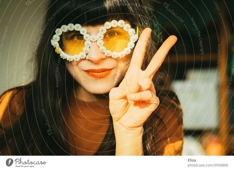 Junge brünette Frau mit sommerlicher Blümchensonnenbrille zeigt das Victoryzeichen Hippie Sonnenbrille pazifistisch Peace peacezeichen zwei ausgestreckte Finger