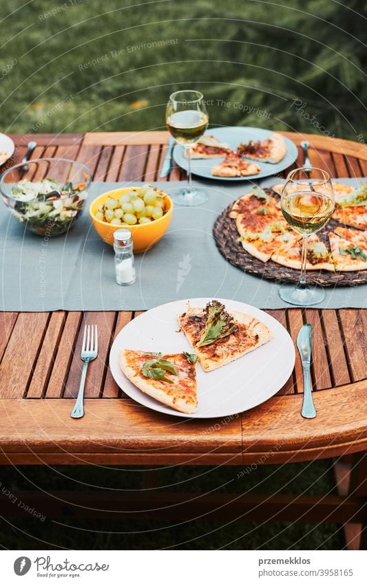 Abendessen in einem Hausgarten. Pizza, Salate, Früchte und Weißwein auf dem Tisch in einem Hinterhof Getränk Feier Speise trinken Essen Festessen Lebensmittel