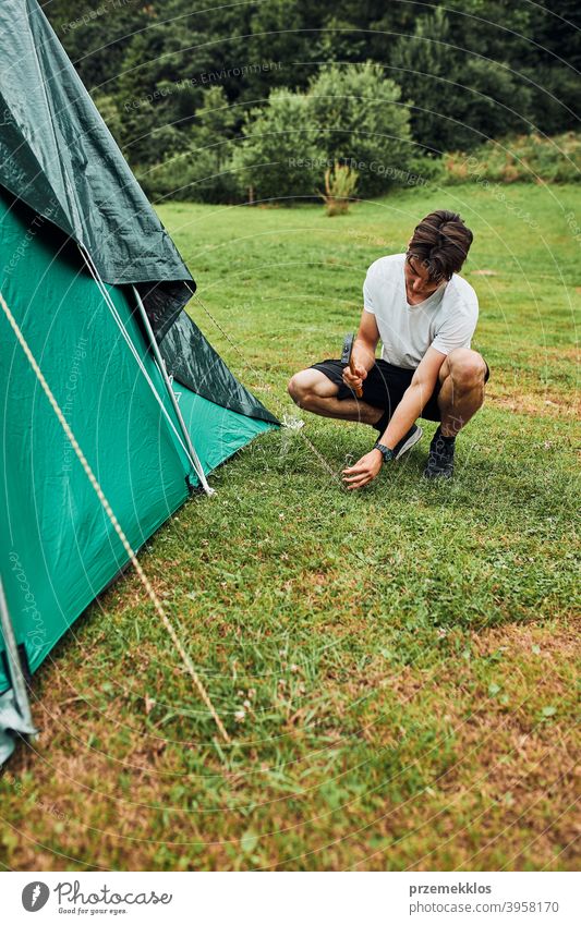 Junger Mann beim Aufbau eines Zeltes auf dem Campingplatz während der Sommerferien Reise Pfahl Zapfen Hammer Gras nach oben Einstellung Setzen Pitsching