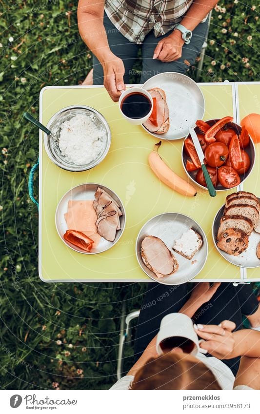 Familie beim Frühstück im Freien auf dem Campingplatz in den Sommerferien authentisch wirklich Banane gekochtes Fleisch langsames Leben Tischdecken im Freien