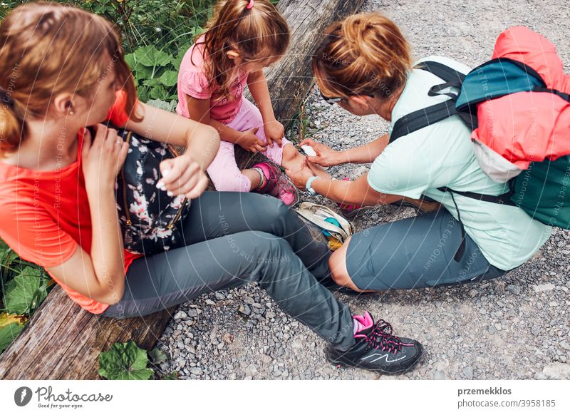 Mutter, die die Wunde am Knie ihrer kleinen Tochter mit Medizin im Spray verbindet. Der Unfall ereignete sich während des Sommerurlaubs der Familie Trekking