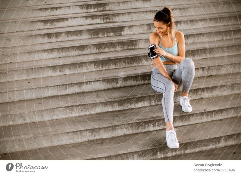 Fitness-Frau, die eine Pause vom Laufen macht, auf den Stufen sitzt und das Handy in der Armbinde verklagt jung Lifestyle urban Training Gesundheit Sport Sitzen