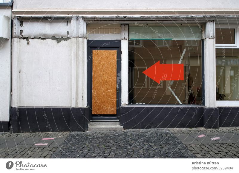 großer roter pfeil am schaufenster eines leeren geschäfts zeigt auf grobspanplatte in der tür laden osb-platte verlassen geschlossen leerstand geschäftsaufgabe