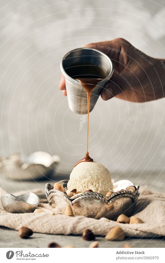 Person, die Karamellsauce auf eine Eiskugel gibt Speiseeis Baggerlöffel Saucen Belag eingießen Dessert süß Leckerbissen Vanille Sahne Schalen & Schüsseln Tisch