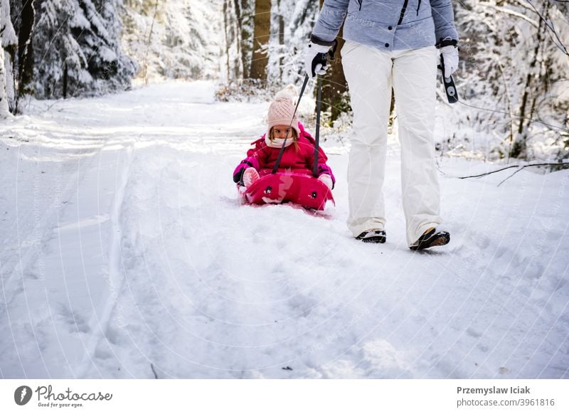 Mutter, die ihr Baby auf einem Schlitten durch den Winterwald zieht. Hintergrund offen Wald Familie authentisch ziehend Kind Person Mädchen Weihnachten Natur