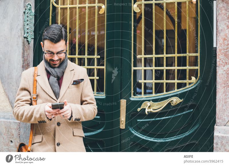 Junger eleganter Mann im Retrostil, der sein Smartphone an der Haustür benutzt jung Schönling Telefon Handy Mobile Stil Mode Straße Porträt