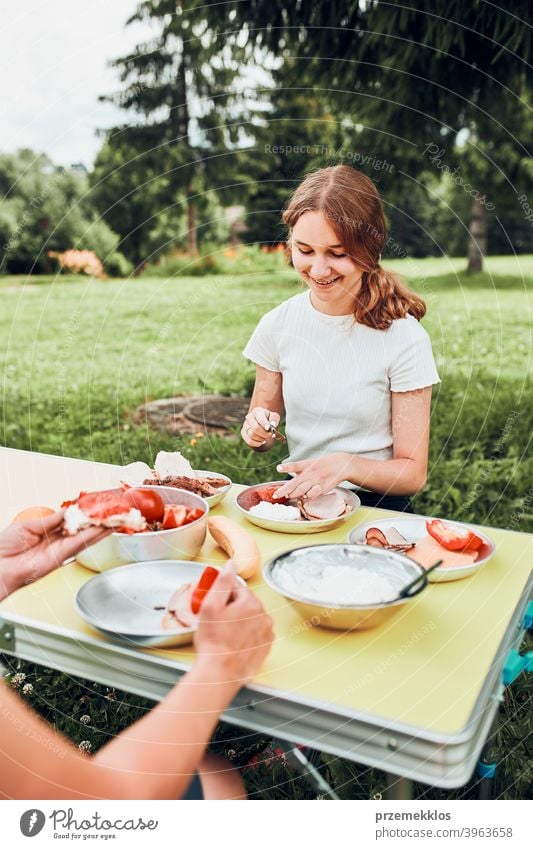 Familie beim Frühstück im Freien auf dem Campingplatz in den Sommerferien authentisch wirklich Banane gekochtes Fleisch langsames Leben Tischdecken im Freien