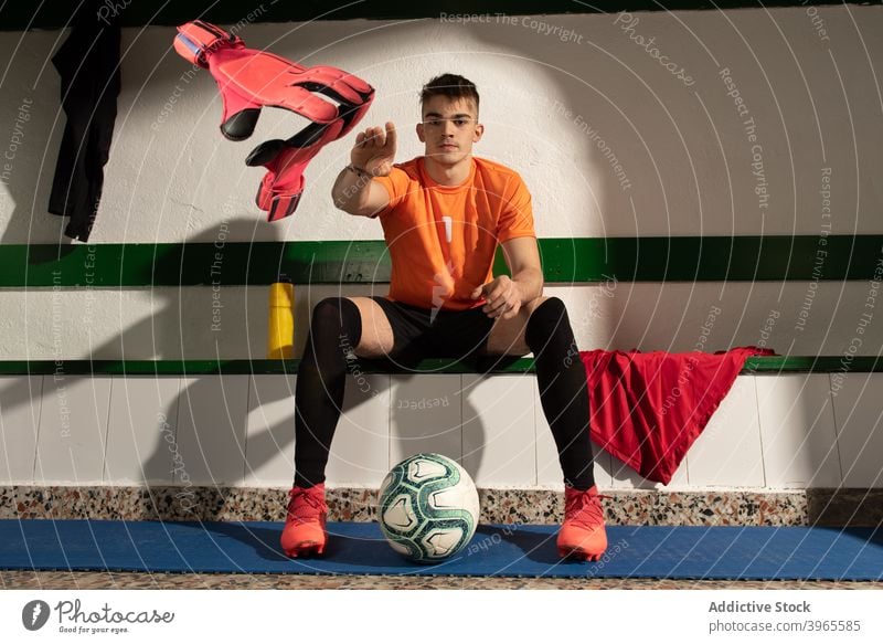 Ein Fußballspieler in der Umkleidekabine mit Sportuniform Mann Spieler sittimg Volk Ankleidezimmer Innenbereich Uniform Turnschuh Bank Sportbekleidung sportlich