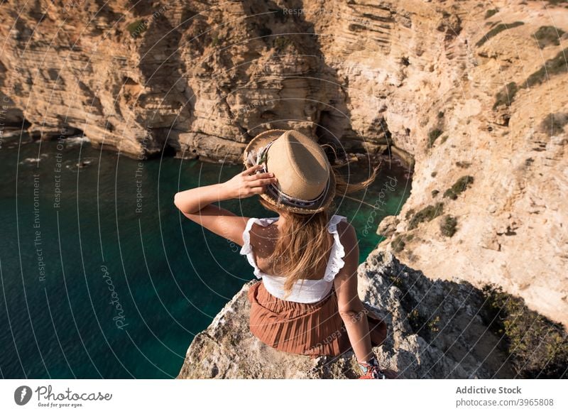 Anonyme Frau in Sommerkleidung sitzt in Klippe Küstenlinie felsig Berge u. Gebirge Feiertage mediterran Horizont bewundernd Seeküste jung Tourismus