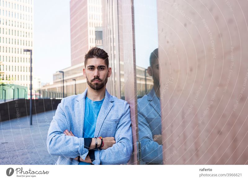 Junger bärtiger Mann mit verschränkten Armen, Model der Mode, im städtischen Hintergrund in lässiger Kleidung cool Stil Porträt Typ 1 photogen stylisch modern