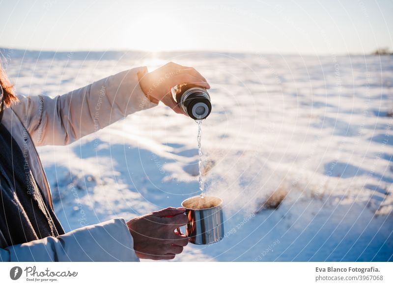 unerkennbar schöne junge Frau bei Sonnenuntergang in verschneiten Berg gießen heißen Tee aus Thermoskanne zu metallischen Tasse. Reisen und Natur Konzept. Wintersaison