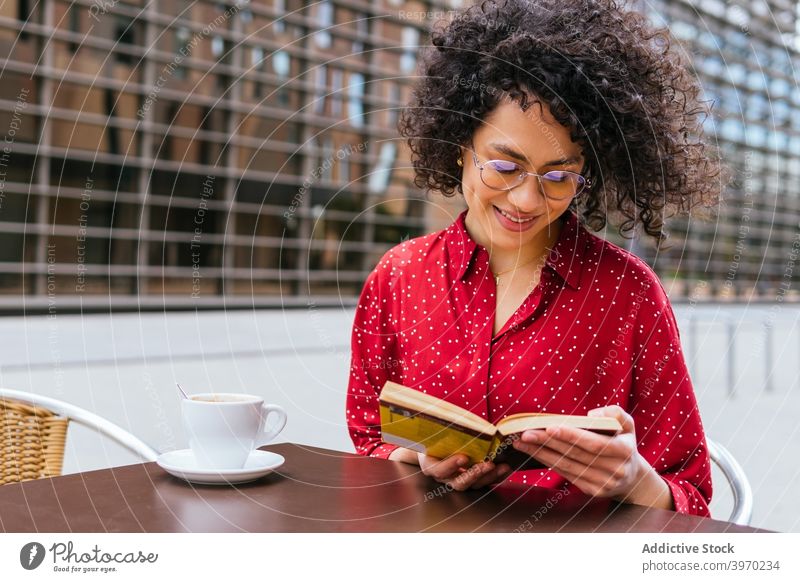 Glückliche Frau liest Buch auf der Terrasse eines Cafés lesen Kaffee ruhen genießen jung positiv ethnisch krause Haare hispanisch Brille interessant Lifestyle