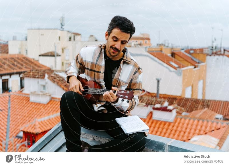 Mann mit Ukulele komponiert Musik auf dem Dach spielen Instrument komponieren Melodie Gesang akustisch Dachterrasse männlich ethnisch Gebäude Konzentration