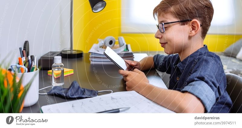 Teenager macht Hausaufgaben mit einem Tablet Blick Tablette Lächeln Heimunterricht Coronavirus Flasche für Handdesinfektionsmittel Maske auf dem Schreibtisch