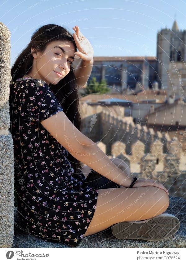 Schöne Frau, die die Sonne mit ihrer Hand verdeckt, sitzt auf einer Mauer Frauen Schönheit weißes Mädchen Kaukasier braune Haare Model Kleid Wand Kathedrale