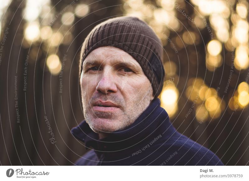 Mann mit Mütze steht vor Waldrand, Bokeh im Hintergrund, ernst beobachtend abwartend Lichter Spaziergang outdoor