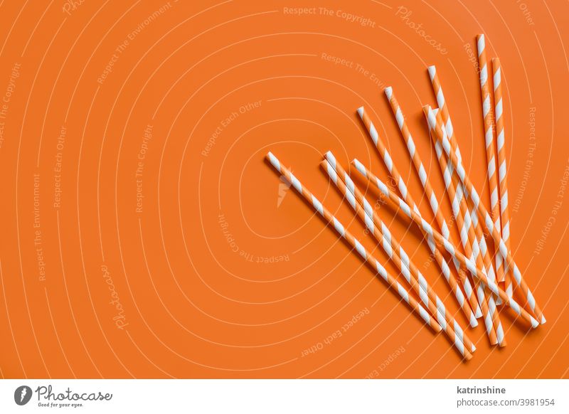 Gestreifte Papier-Trinkhalme auf orangem Hintergrund von oben gestreift trinken Strohhalme abbaubar Textfreiraum Draufsicht umweltfreundlich Cocktail Monochrom