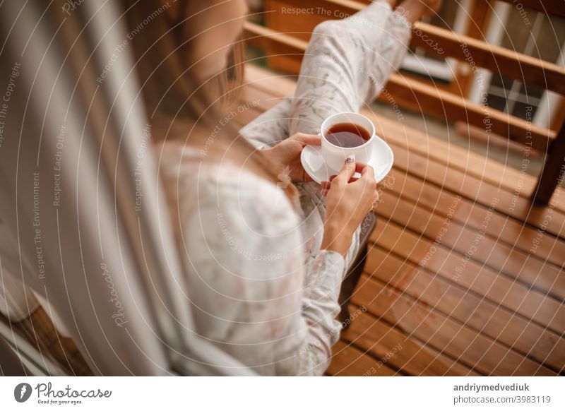 Junge Frau in stilvoller Nachtwäsche trinkt morgens gerne Kaffee oder Tee im Freien auf dem Balkon und schaut auf die Berge. Tasse heimwärts