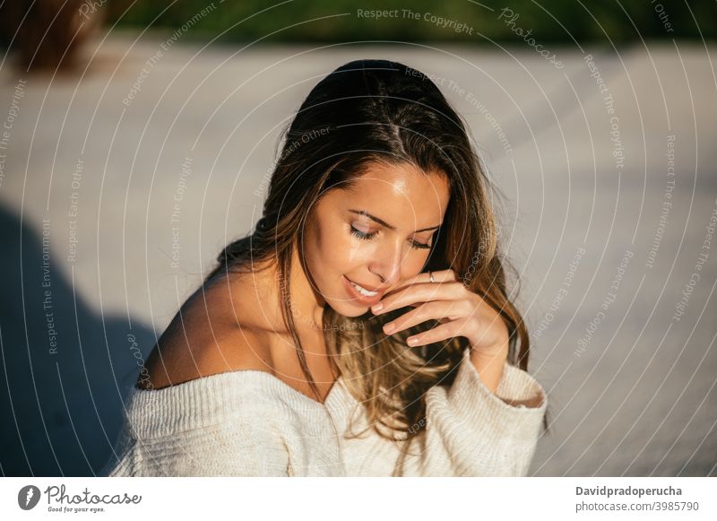 Glückliche junge Frau in modischem Pullover Lächeln ruhen Hof Stil Gesicht berühren Augen geschlossen Angebot Vorschein lange Haare gestrickt weich Freude