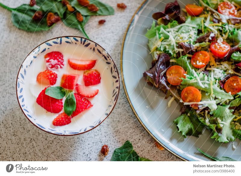 Nahaufnahme einer gesunden Mahlzeit aus Joghurt mit Erdbeeren, begleitet von einem Teller mit frischem Salat. Lebensmittel Gesundheit erdbeeren Tomaten