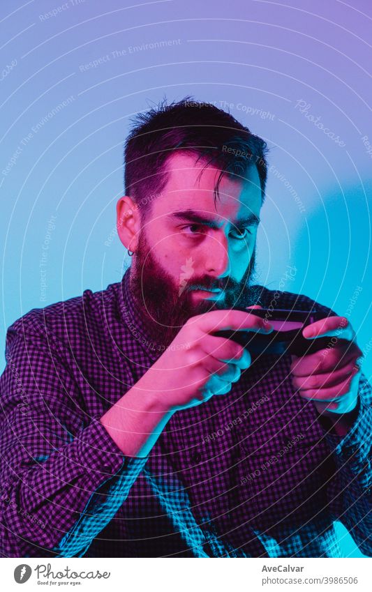 Ein junger Hipster-Mann hält ein Konsolen-Pad, während er mit einem ernsten Gesicht mit rosa und blauen Lichtern spielt 20s Kopierbereich aufregend Videospiel