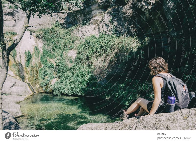 Mädchen sitzt auf einem Felsen und schaut auf eine Landschaft mit einem kleinen Wasserfall friedlich Gelassenheit Frieden Ruhe Erkundung meditieren rein