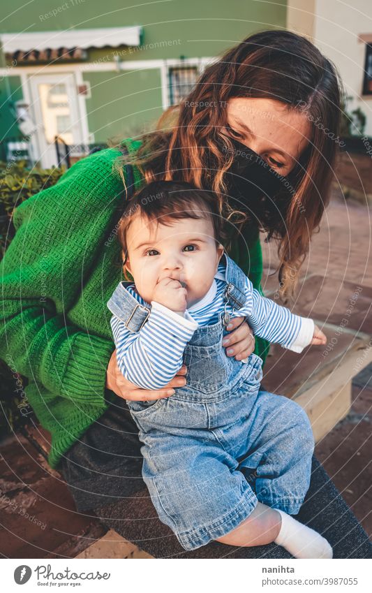 Bild in Grüntönen einer jungen alleinerziehenden Mutter mit ihrem Baby während der Covid-Pandemie COVID Coronavirus Familie Mutterschaft Mama Mundschutz