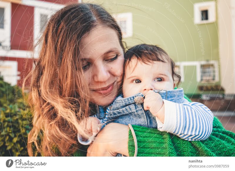 Liebliches junges Baby in den Armen seiner Mutter Familie Mutterschaft Mama grün urban lange Haare Zeit Trave Feiertage Jeanshose lässig anhaben junge Mutter