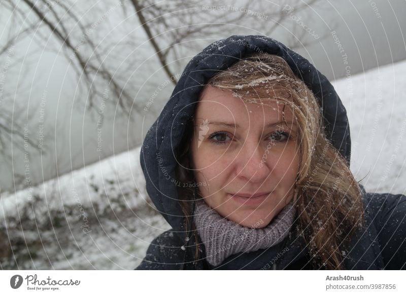 Junge Frau im Schneefall mit Kapuze (Selbstportrait) sportlich Bewegung Erholung kalt Winter schneeflocken Augen Nase Mund lange Haare Blond blau Jacke