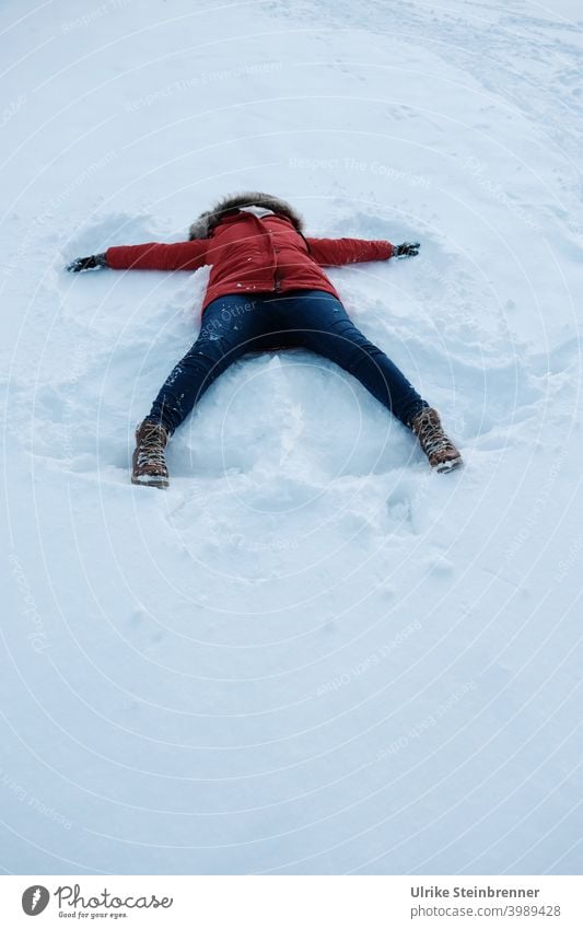 Frau in rotem Anorak macht einen Schneeengel Winter Spaß Neuschnee Winterspaß Engel Engelsflügel Abdruck Wiese Schneedecke weiß kalt Kapuze Wetter Beine Jeans