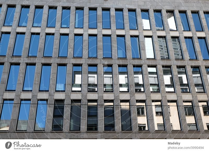 Spiegelnde blaue Fenster in grauem Beton eines modernen Bürogebäude im Sommer bei Sonnenschein in der City von Frankfurt am Main in Hessen Architektur Fassade