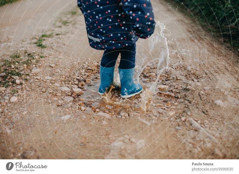 Kind mit roten Gummistiefeln spielt auf einer Pfütze Winter Regen Wasser nass Mensch Außenaufnahme Farbfoto Spielen Freude Stiefel dreckig Schlamm Kleinkind