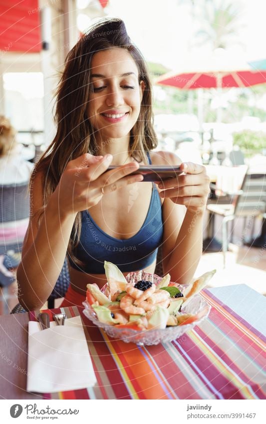 Junge Frau, die ihren Salat mit einem Smartphone fotografiert, während sie in einem Restaurant sitzt Lebensmittel Salatbeilage Gesundheit Telefon Mobile