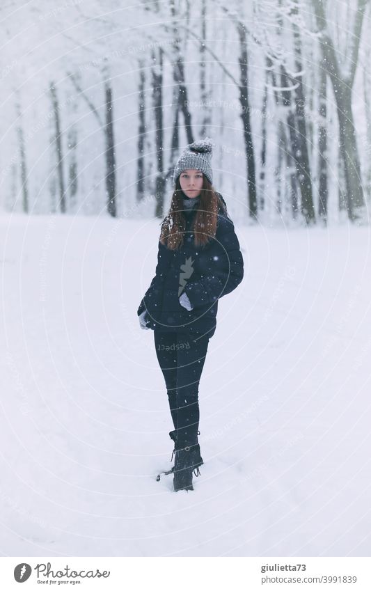 Porträt eines Teenager Mädchens im Winter bei Schneefall stehend in einem verschneiten Park Vorderansicht Blick in die Kamera Farbfoto Jugendliche Außenaufnahme