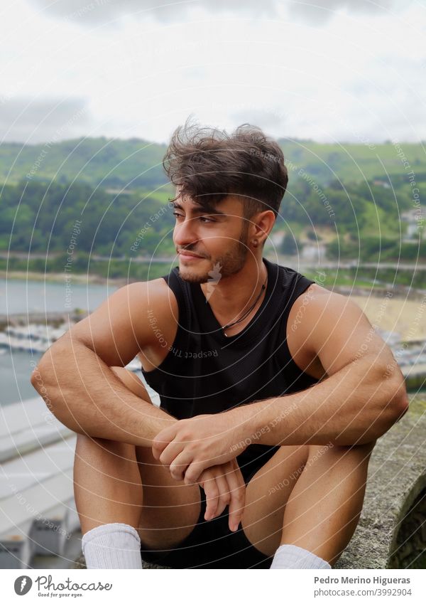 Hispanischer Mann sitzend, posierend, mit verblasstem Haar und Bär, der ein Basketball-T-Shirt trägt Model kein Blick jung schön Korb-T-Shirt Erwachsener