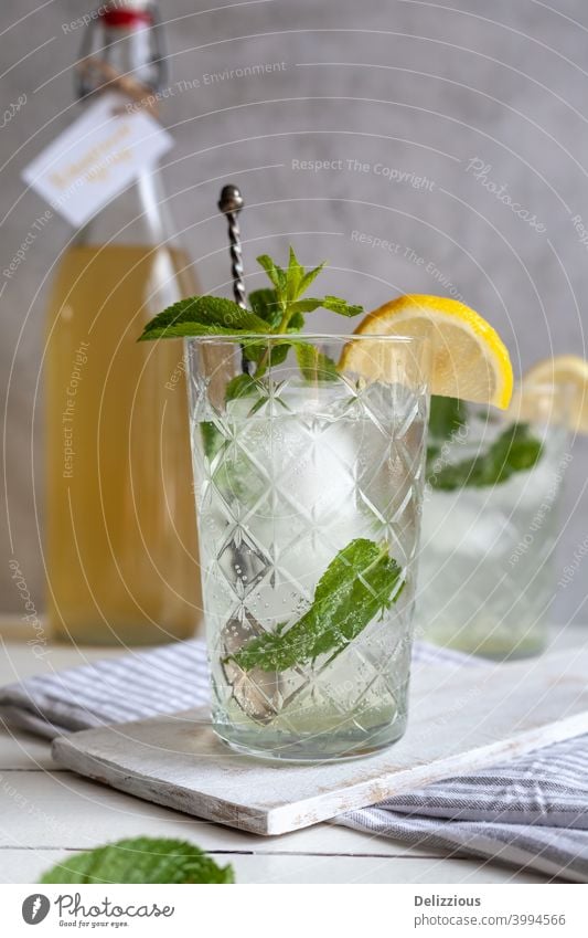 Erfrischendes Limonadengetränk mit Eis, Zitrone und Minze mit Sirupflasche im Hintergrund Getränk Blütezeit Flasche sprudelnd Zitrusfrüchte Cocktail kalt cool