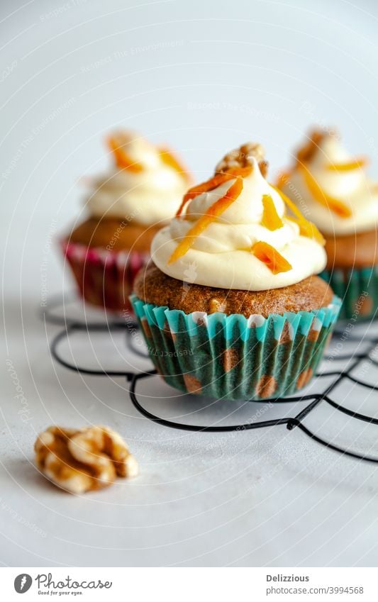 drei Karottenkuchen Muffin mit Zuckerguss und Karotte Rasur auf Kühlregal weißem Hintergrund backen Bäckerei Geburtstag blau hell braun Kuchen Möhre Feier Zimt