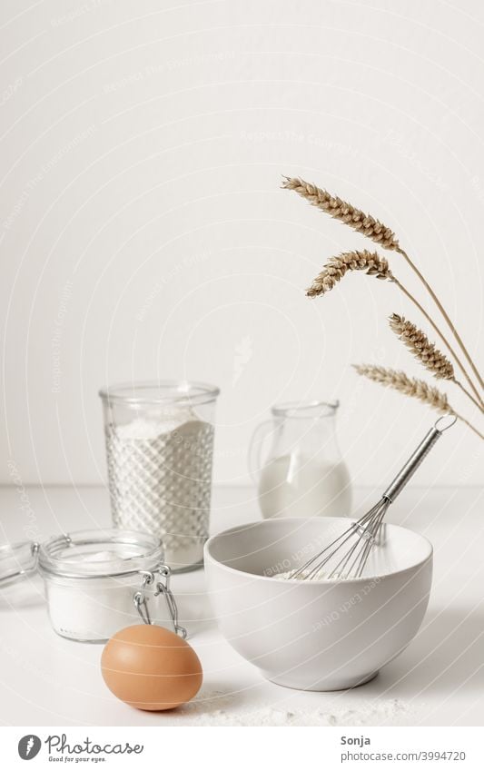 Mehl in einer Schüssel und Backzutaten auf einem weißen Tisch Zutaten backen Ei weißer Hintergrund Weizenähre Küche Vorbereitung roh Essen zubereiten frisch