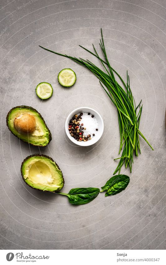 Eine Schüssel mit Salz und Pfeffer und grünes Gemüse und eine halbierte Avocado im Kreis. Rustikaler Hintergrund roh Flat lay rustikaler Hintergrund Gesundheit