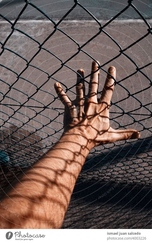 metallische Zaunschatten auf der Männerhand Hand Arme Körperteil Haut Schatten Formen Finger Handfläche Handgelenk Stahl Metall Straße im Freien packend