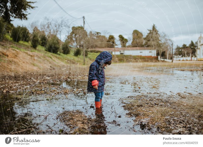 Kind mit roten Gummistiefeln spielt auf einer Pfütze Kindheit Regen authentisch Mensch Spielen Wasser nass Außenaufnahme Freude Farbfoto Stiefel Fröhlichkeit